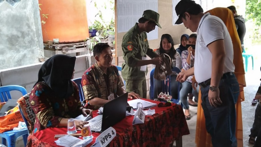 Ketua DPRD Balikpapan Abdulloh (kaos putih) menyerahkan HP dan tasnya kepada petugas Linmas sebelum mencoblos di TPS 55 Batu Ampar. (Hendra/KoranKaltim.Com)