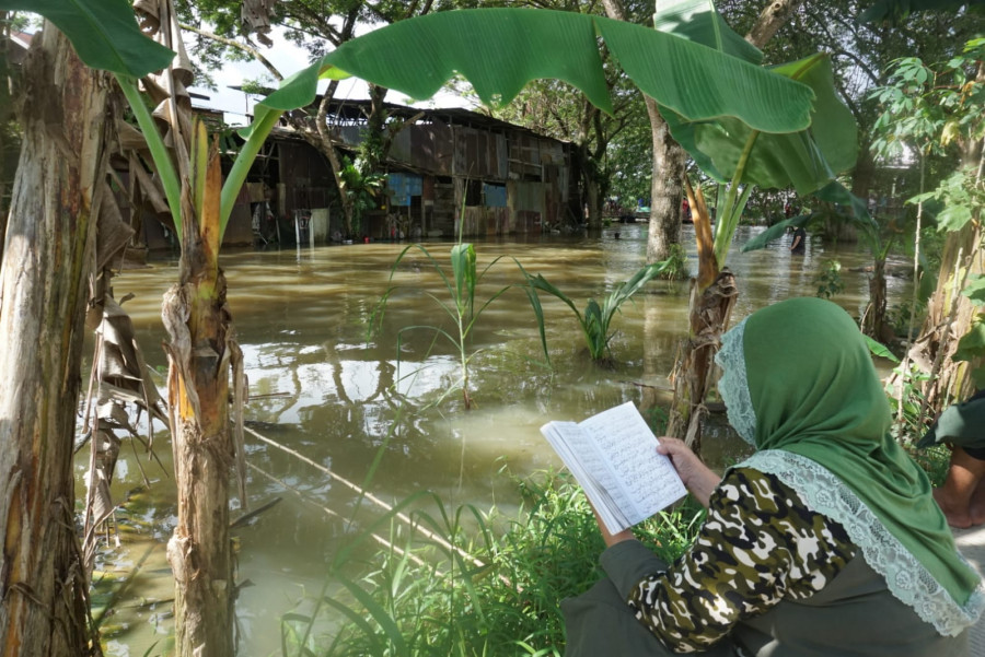 Nenek korban Siah (65) yang tengah duduk di pinggir sungai, sambil membaca yasin untuk cucunya, dan berharap MF (11) bisa segera ditemukan dalam kondisi selamat Kamis (2/9/2021) hari ini. (Foto:Nancy/korankaltim.com)