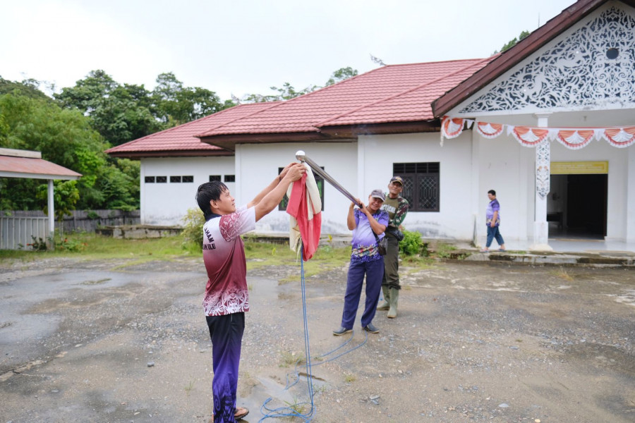 Personel satgas TMMD bantu pegawai Kecamatan turunkan bendera tersangkut. (Foto: Humas Kodim)