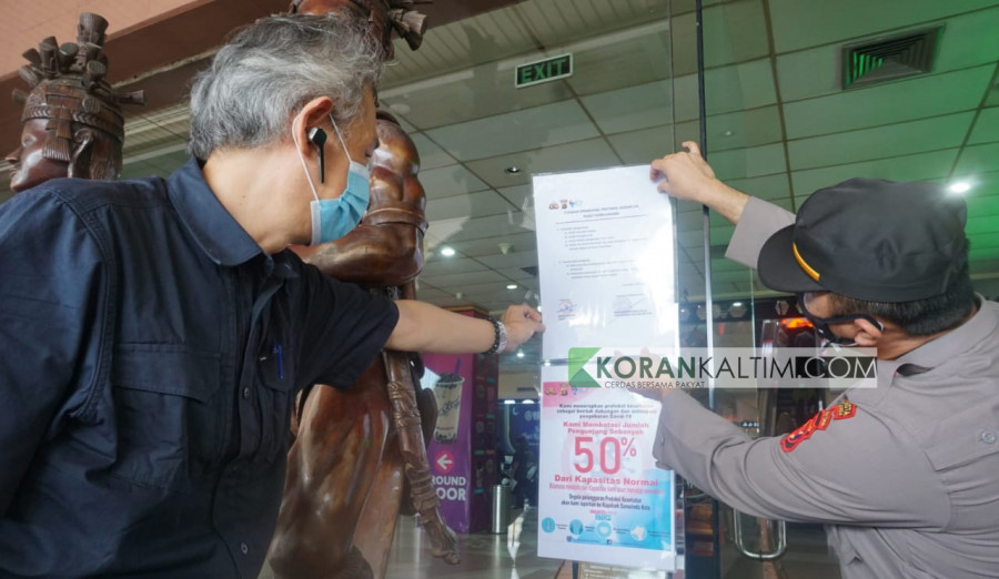 Kapolsek Samarinda Kota AKP Creato Sonotehe Gulo (kanan) saat memasang serta imbauan terkait SOP masuk ke mal Kamis (6/5/2021) hari ini. (Foto:Nancy/korankaltim.com)
