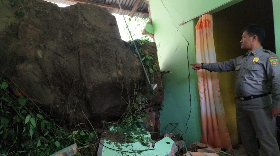Petugas Satpol PP Samarinda saat menunjukkan bongkahan tebing yang membuat jebol diding rumah milik Iman Sujito (61) tadi malam. (Foto: Nancy/korankaltimcom)