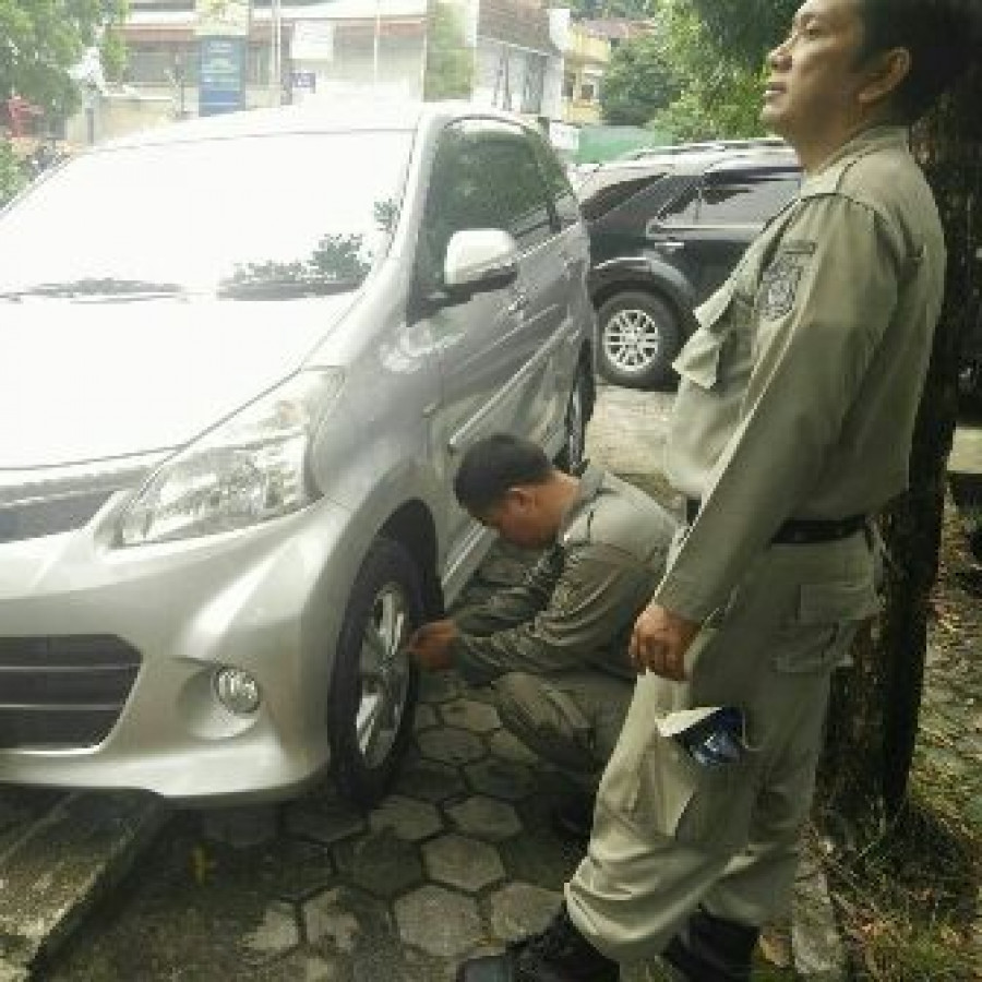 PETUGAS Satpol PP saat menggembosi ban mobil yang masih saja parkir di atas trotoar.