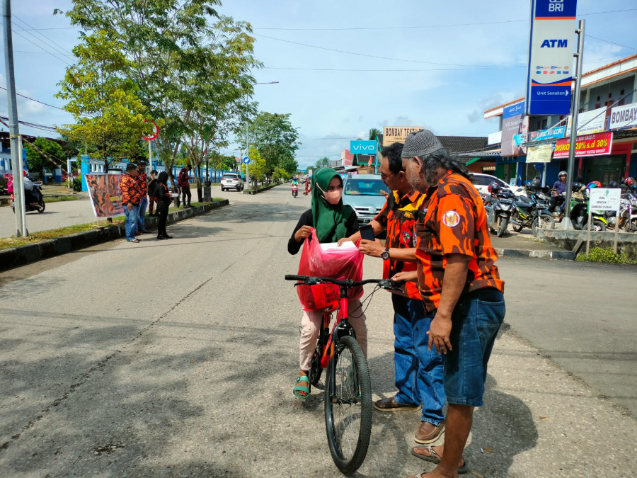 Ketua MPC Pemuda Pancasila Kabupaten Paser Hotman Butar-Butar (pakai kacamata) saat membagikan nasi kotak kepada pengendara. (Foto : Dwi Cahyo / Korankaltim.com)